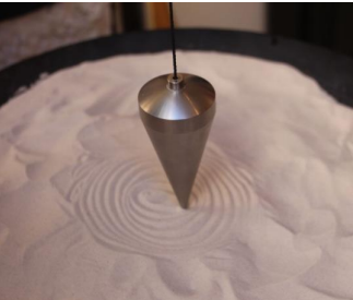 Pendule en métal suspendu au-dessus d'un plateau de sable avec cercles concentriques tracés