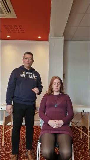 Praticien debout derrière le receveur assis, posture calme et centrée